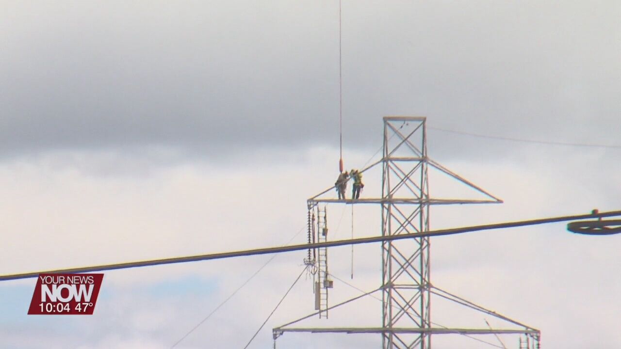 Power line workers soar through the sky hanging from a helicopter in Allen County